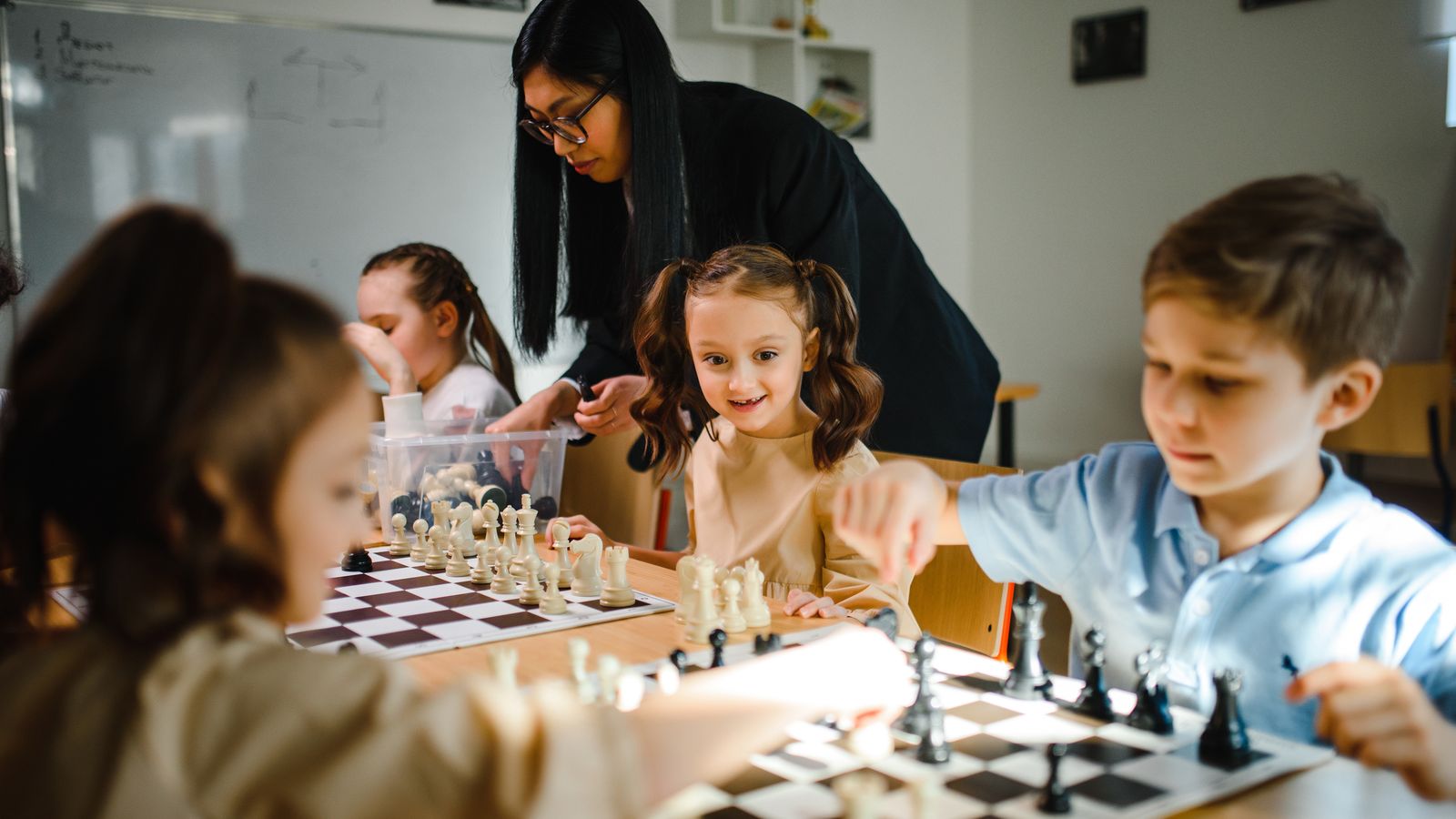 Children playing chess with their teacher in a school club session